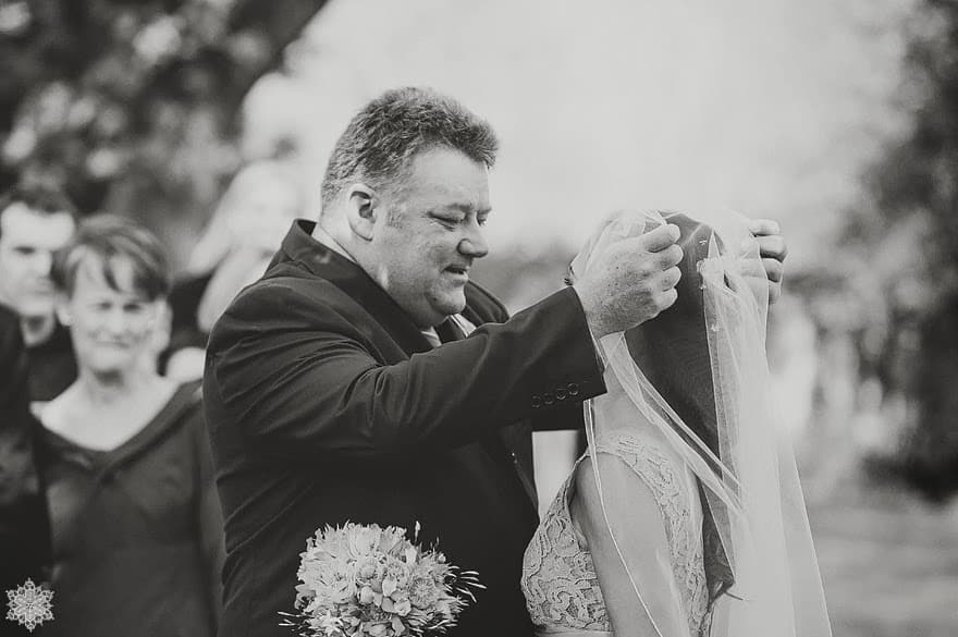 A father lifting his daughter's veil moments before the ceremony