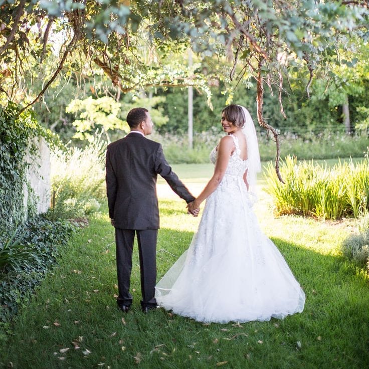 A bride and groom walking hand in hand through the shaded Manor garden at Muldersvlei