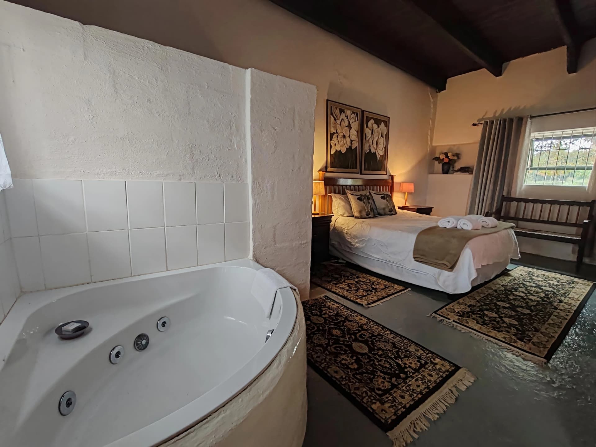 A Muldersvlei guest room with a corner spa bath, made-up bed and woven rugs on the floor