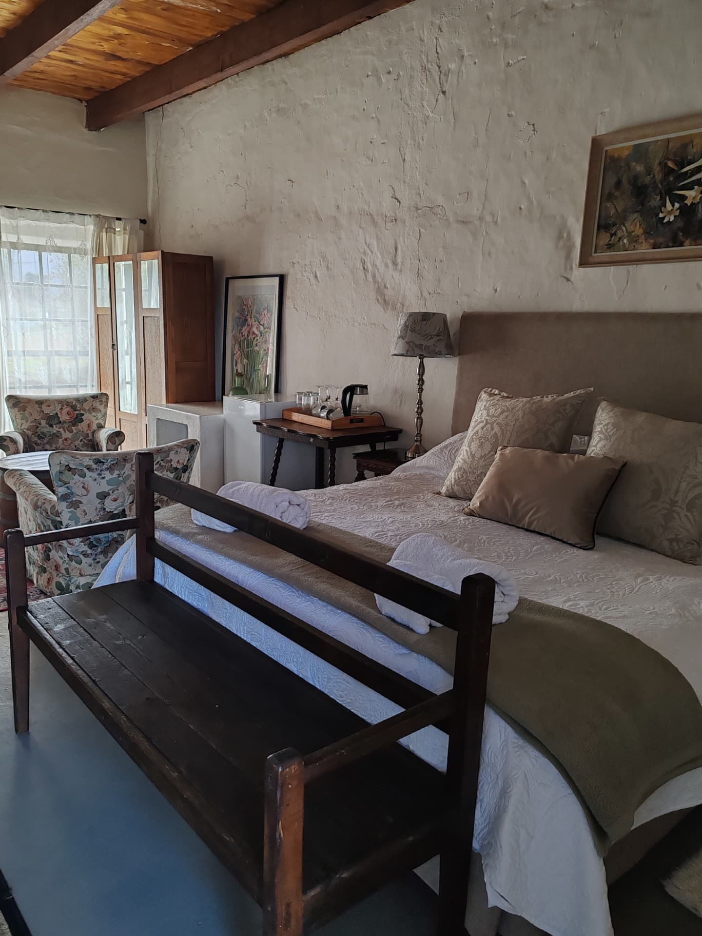 A real Muldersvlei guest room with a dark riempie bench, floral armchairs and morning light through the shutters